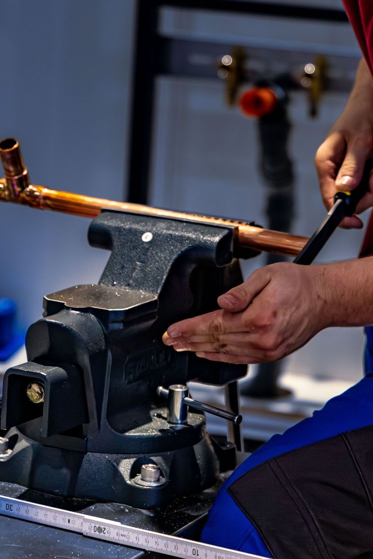 Plumber's hands working on a length of copper pipe held in a bench vice
