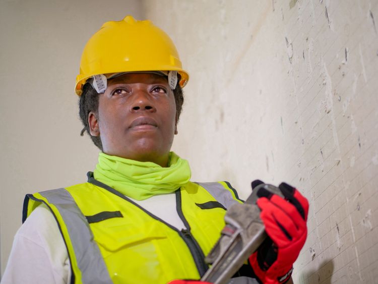 Plumber in a hard hat and hi-vis vest holding a pipe wrench